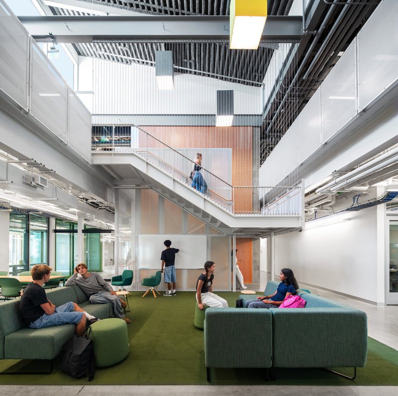 Interior courtyard with green modular seating and students beneath corrugated metal balconies and open ceiling