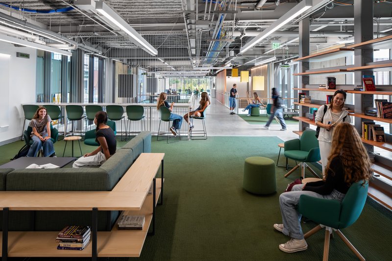 Open workspace with green lounge seating, exposed ceiling systems, and students gathered throughout the space