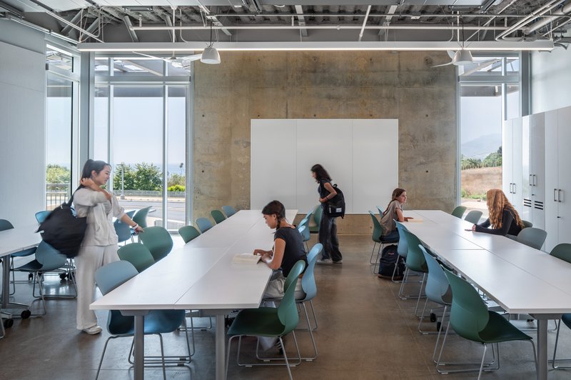 Meeting room with white tables, green chairs, concrete wall, and whiteboard mounted against exposed services