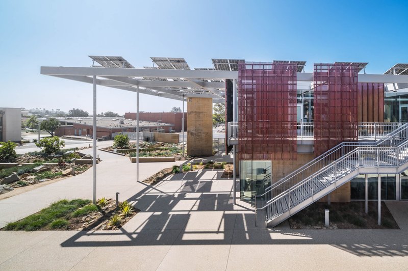 Exterior stair with metal railings ascending to upper level beneath a cantilevered solar panel canopy
