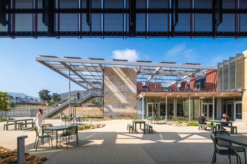 Courtyard terrace with tables and people gathering beneath perforated metal canopy and solar panel array