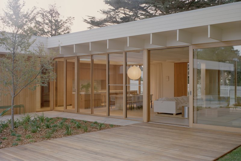 Timber deck extending from floor-to-ceiling glass doors with planted bed along the side