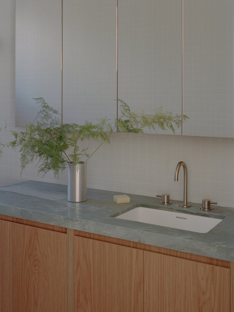 Oak vanity with green stone countertop and undermount sink beneath white tile backsplash and upper cabinets