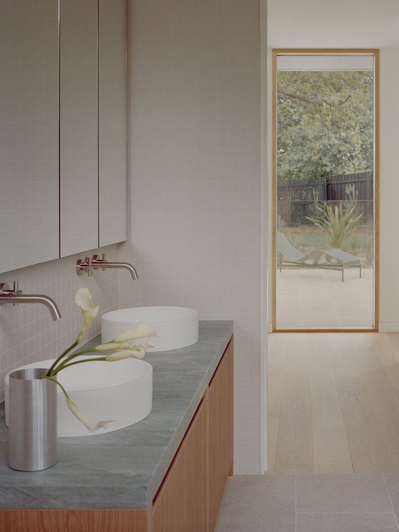 Bathroom vanity with twin vessel sinks and timber-framed window overlooking a garden courtyard