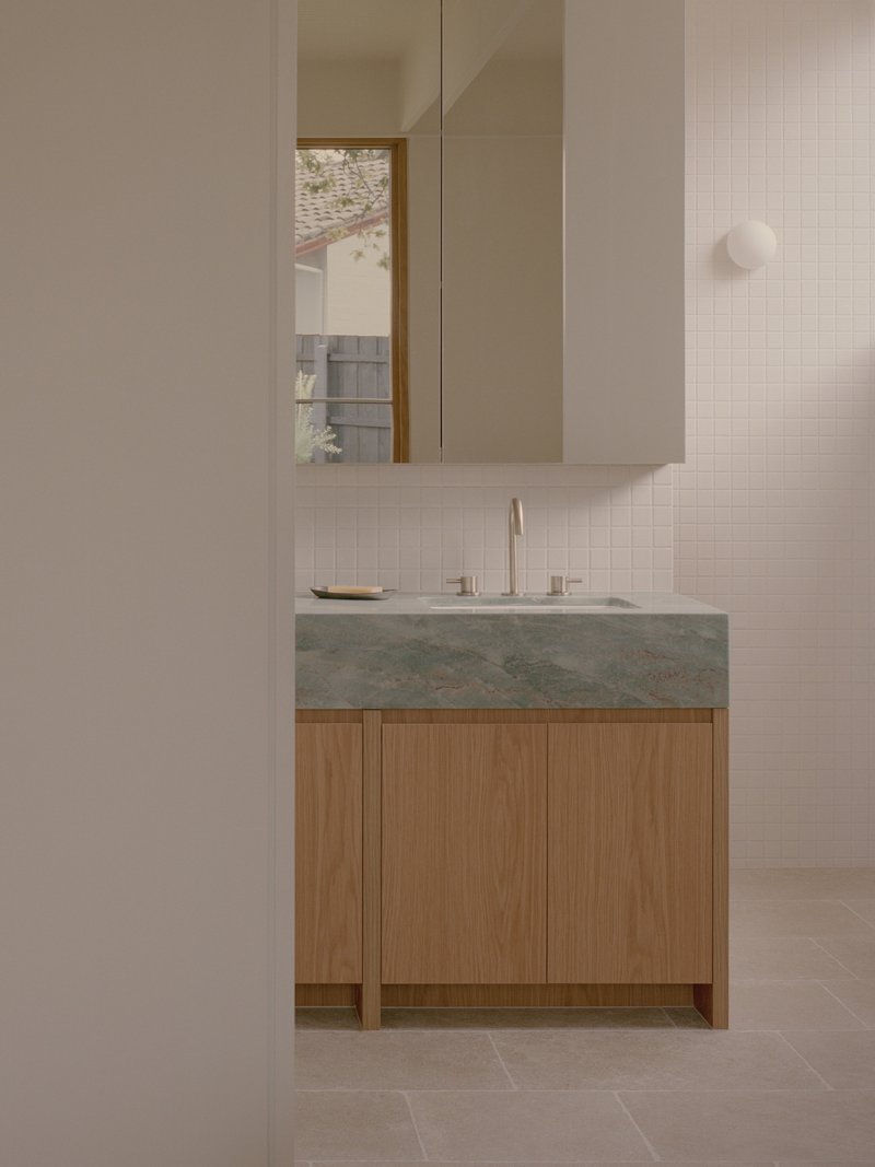 Floating oak vanity with integrated green stone counter below white wall cabinets and medicine mirror