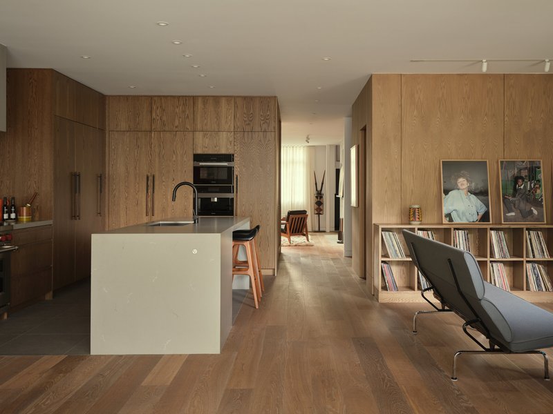 Open kitchen with white island and dark oak cabinetry, looking through to a corridor with vinyl storage