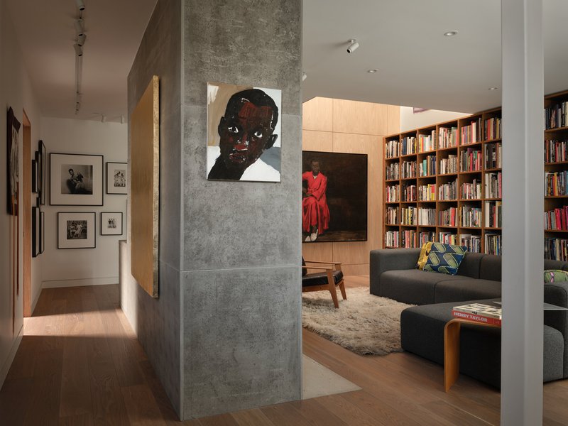 View through concrete column toward living area with floor-to-ceiling bookshelf in warm interior light