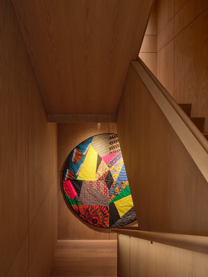 Wood-paneled staircase with patchwork quilt displayed in a recessed niche beneath the landing