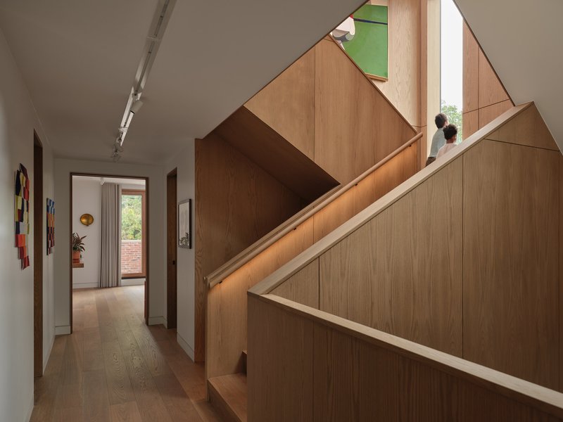 Oak staircase rising from hallway with two figures ascending toward a stained glass window