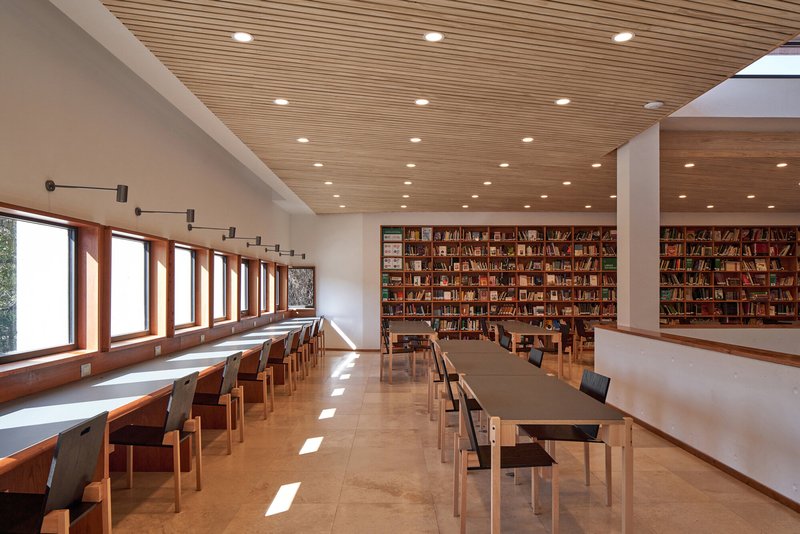 Reading room with timber slat ceiling, bookshelves along one wall and long study tables receiving daylight