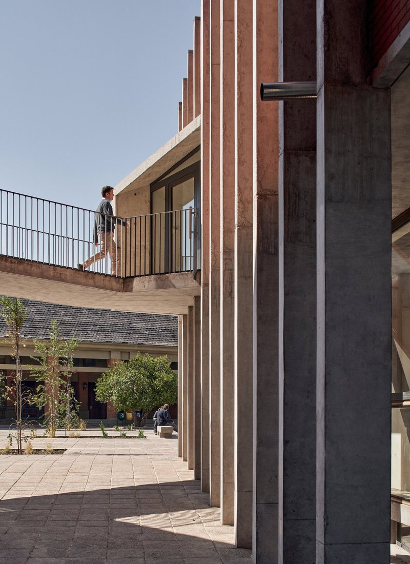 Detail of concrete columns and red brick fins framing a person on the elevated terrace