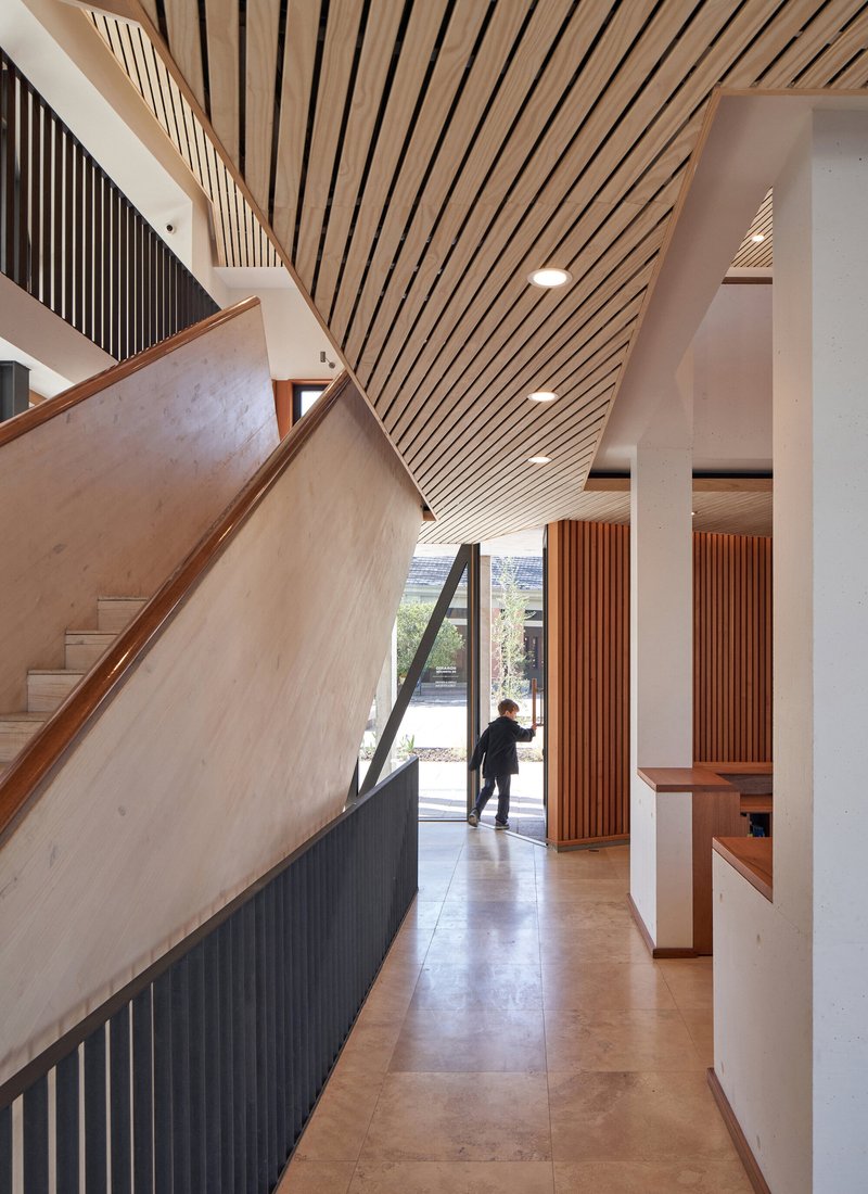 Entry hall with diagonal timber ceiling slats and a person approaching the glazed door