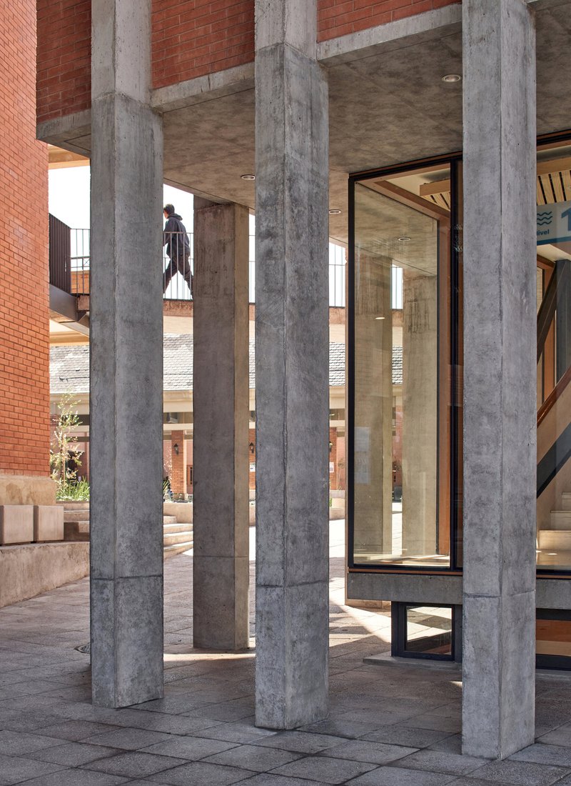 Exterior colonnade of board-formed concrete columns framing a glass door with a figure visible beyond