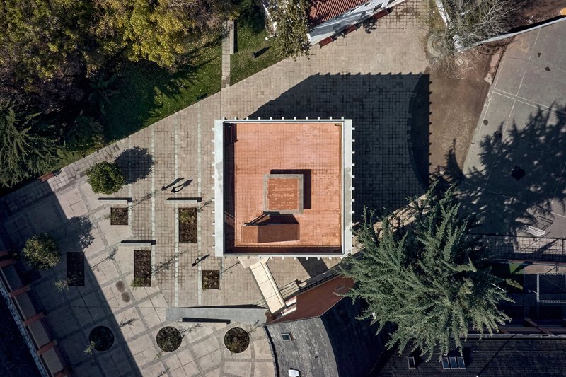 Aerial view of a courtyard with light and dark paving, circular planters and tree shadows