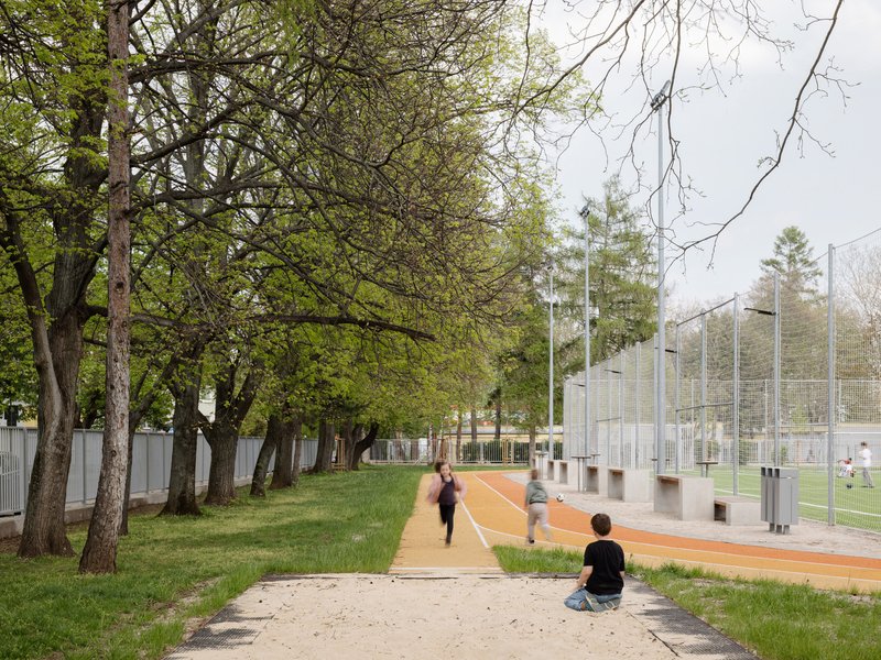 Tree-lined path alongside the sports court with people running and sitting