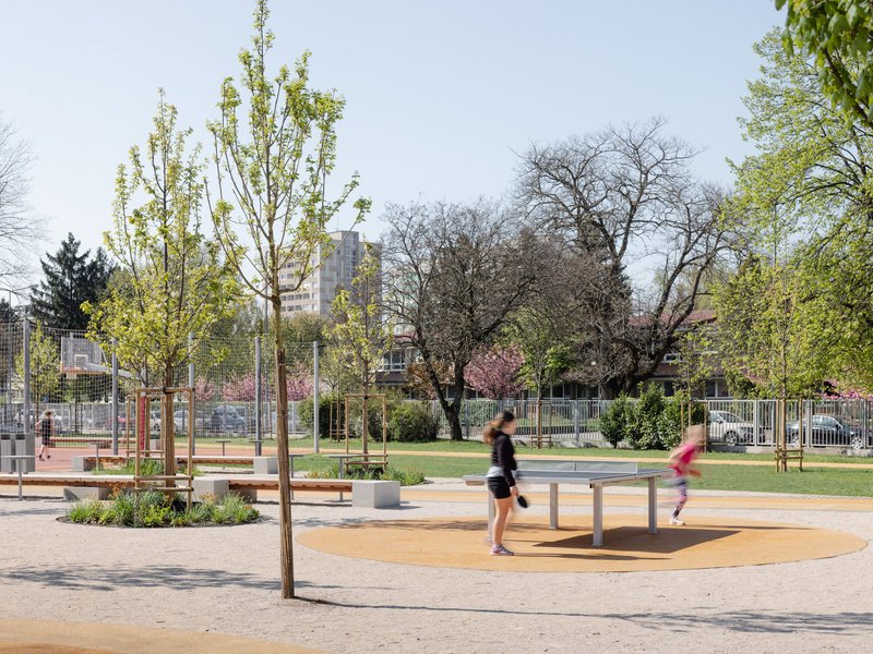 Paved plaza with planted beds and timber benches as joggers pass through in daylight