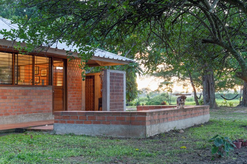 Exterior corner showing red brick walls and concrete plinth beneath a metal roof and overhanging tree canopy