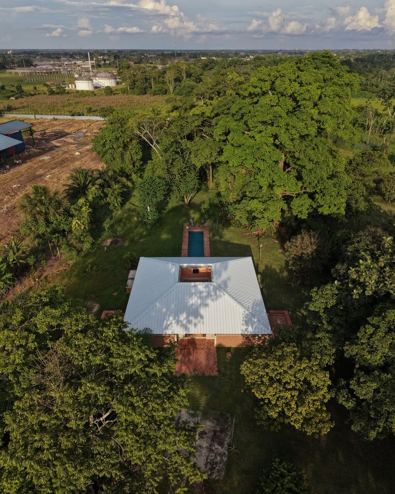 Aerial view of the gabled metal roof surrounded by dense tree cover and open farmland beyond