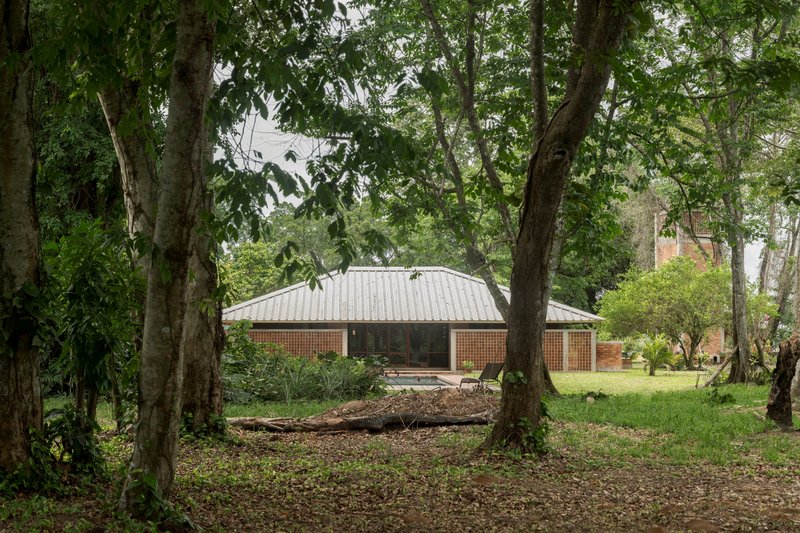 Single-story pavilion with corrugated metal roof and latticed brick screens nestled among mature trees