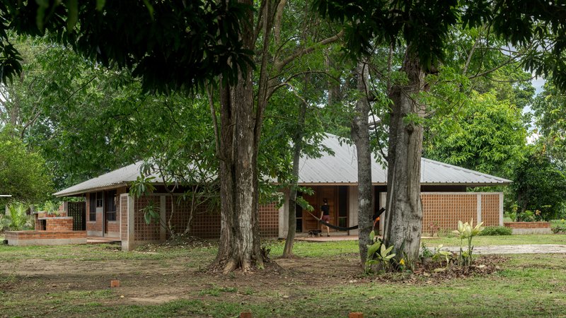 Low-slung residence with hip roof and perforated brick facade viewed through a grove of tall trees