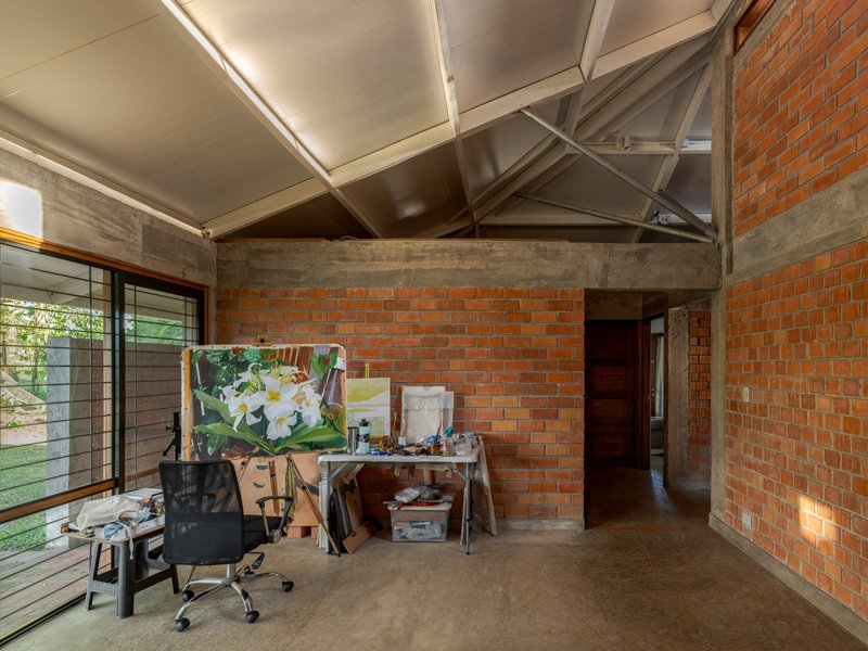 Interior studio space with exposed steel roof trusses, brick walls and an easel beside horizontal windows