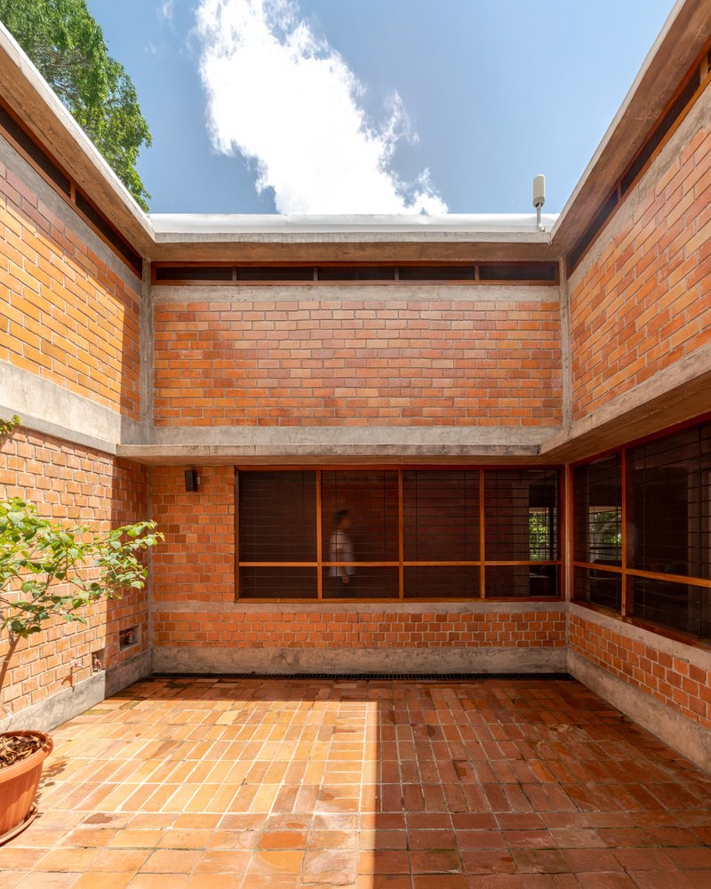 Interior courtyard with terracotta brick paving and walls surrounding timber-framed glazing under open sky