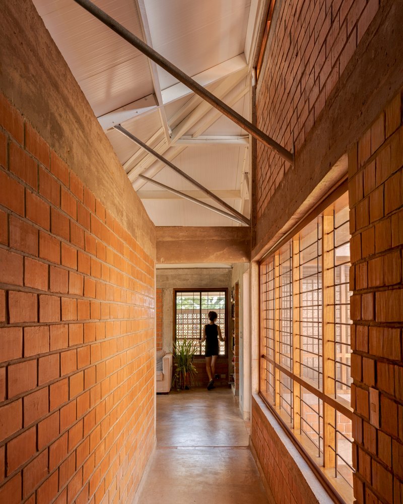 Corridor with exposed brick walls and gridded wood screens filtering warm afternoon light toward a figure