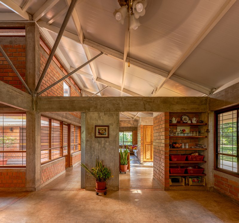 Open interior space with exposed concrete beams, timber-lined ceiling, and brick infill walls in afternoon light