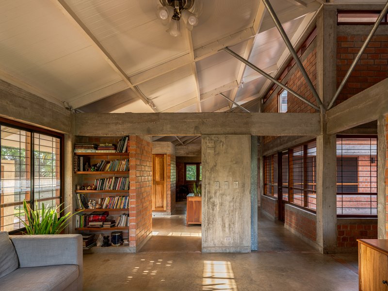 Living area with board-formed concrete columns framing views through timber-louvred windows to adjacent spaces