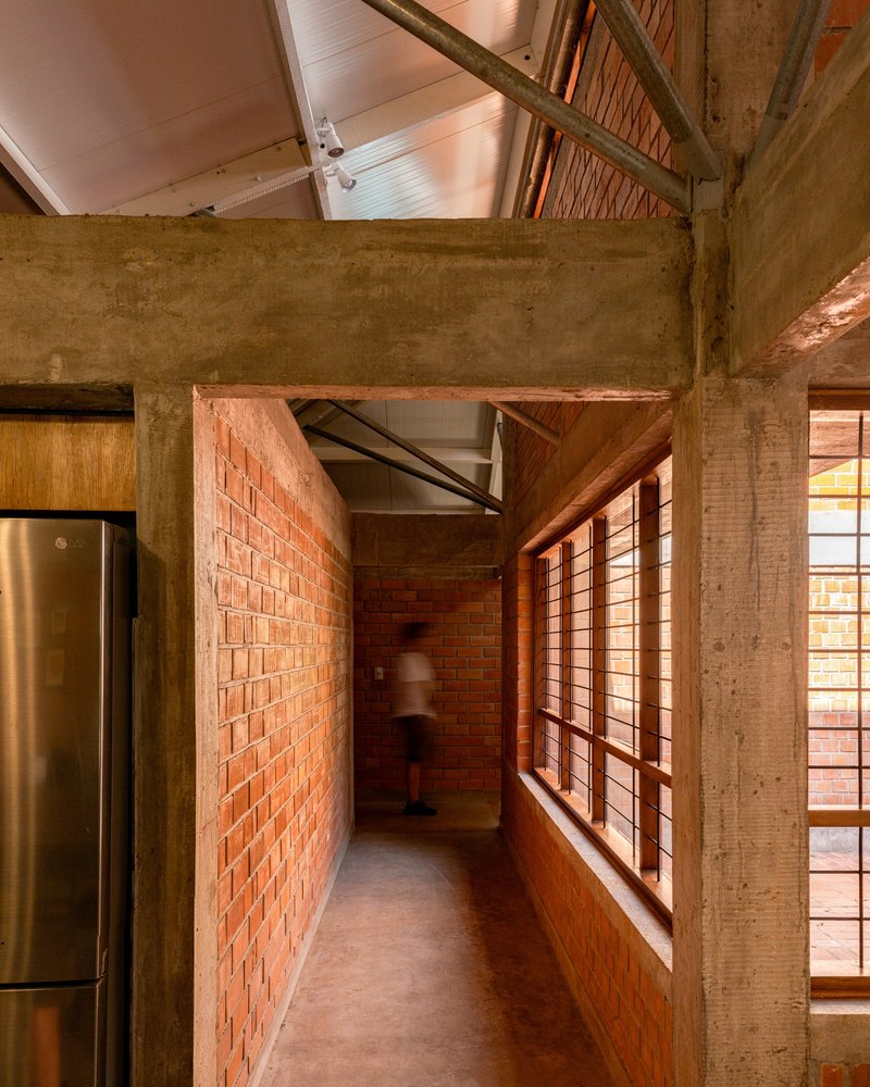 Corridor with exposed brick wall and concrete beam framing a figure in motion beneath the roof structure