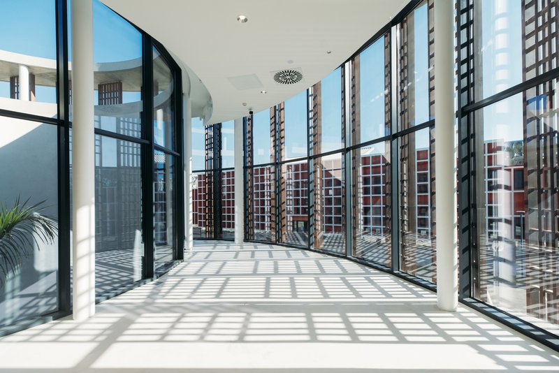 Interior corridor with floor-to-ceiling glass walls and patterned light cast by exterior screens