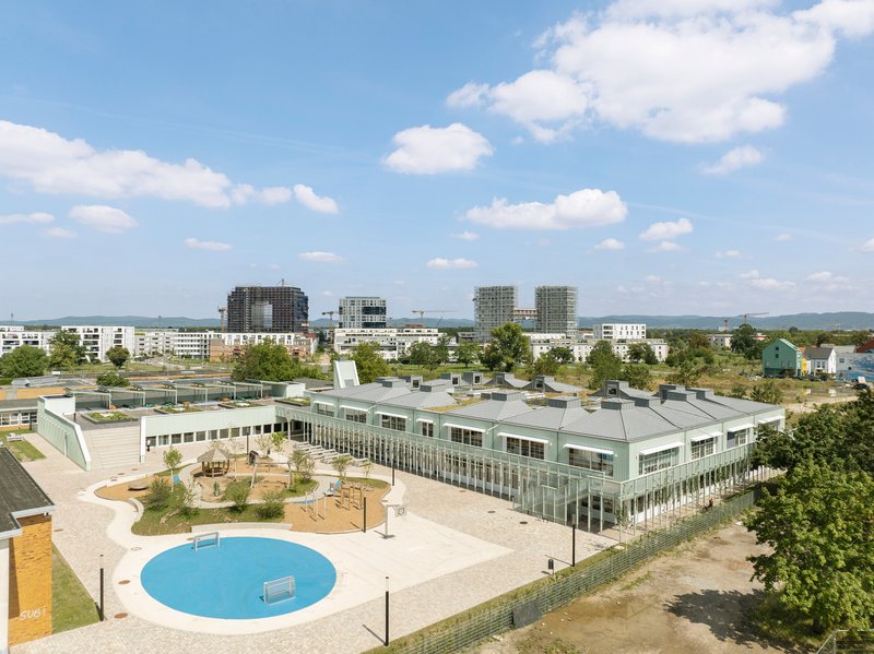 Aerial view of the pale green corrugated roofscape with circular blue pool in the foreground plaza
