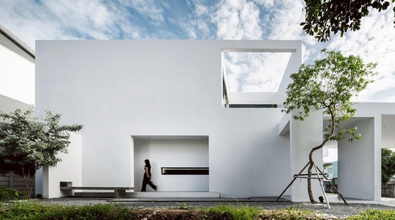 White stucco facade with rectangular voids and recessed entry as a figure walks through the courtyard
