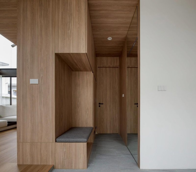 Entry hallway clad entirely in timber veneer with built-in bench and grey stone flooring