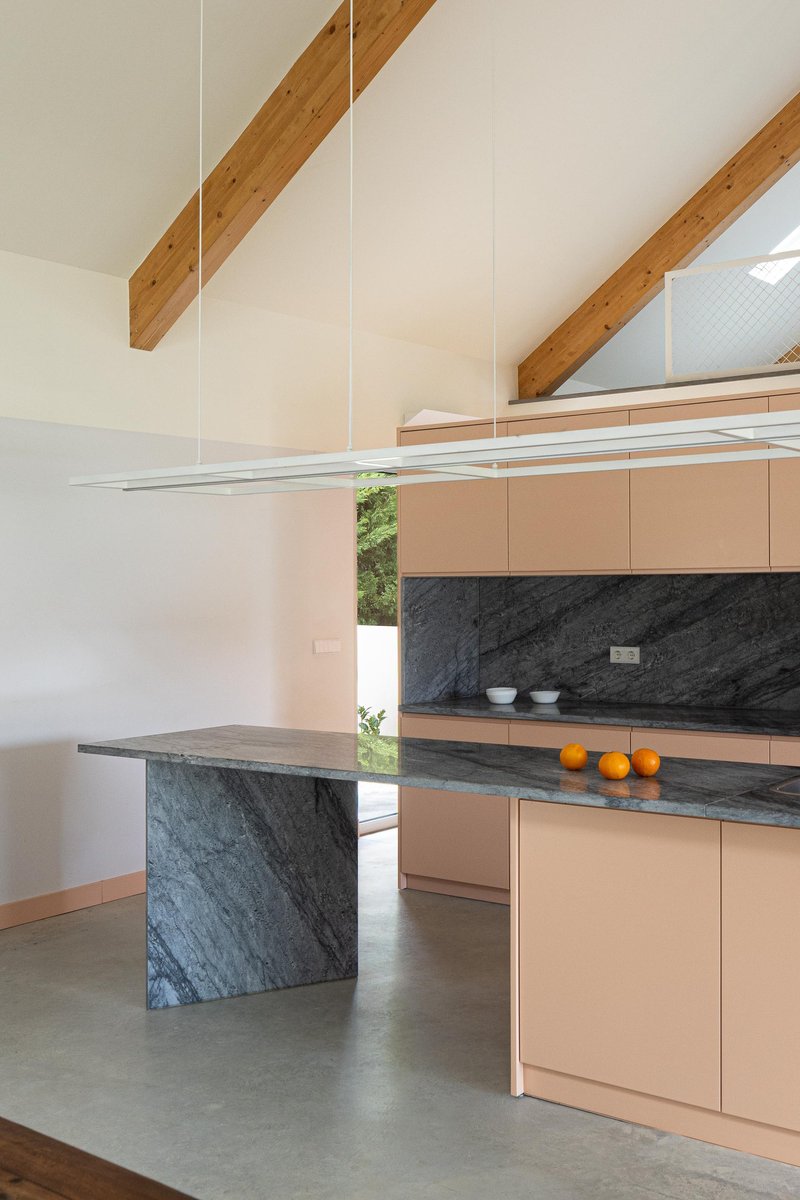 Kitchen with pale pink cabinets, black marble island and backsplash, exposed timber beams overhead