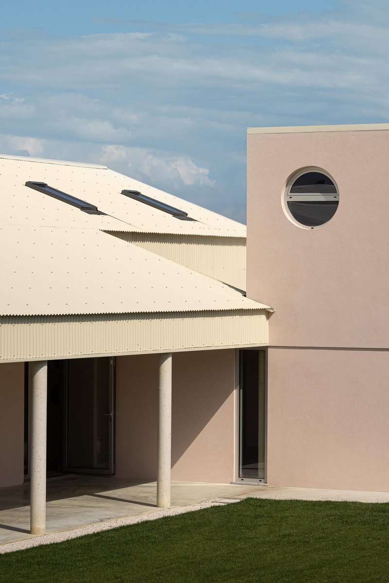 Junction between the corrugated metal roof and pink-rendered wall with circular window under afternoon light