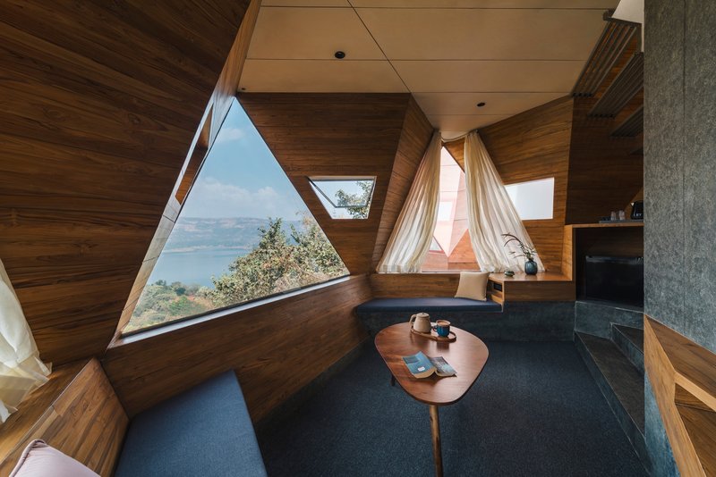 Sitting area with timber-clad angular walls and triangular window framing a distant lake view