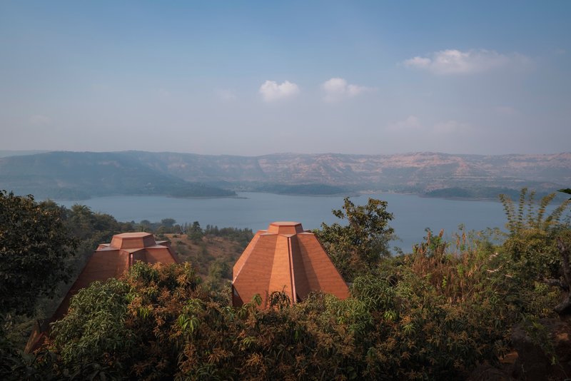 Distant view of red terracotta pyramidal roofs emerging from trees overlooking a wide reservoir and hills