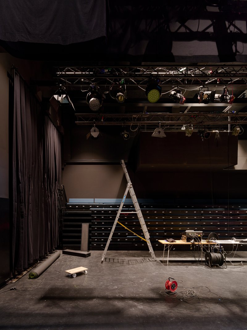 Stage area with lighting rig overhead and ladder resting among scattered equipment on concrete floor