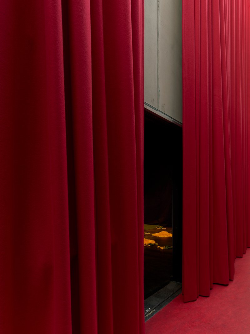 Deep red fabric curtains parted to reveal a dark theater space with painted floor visible beyond