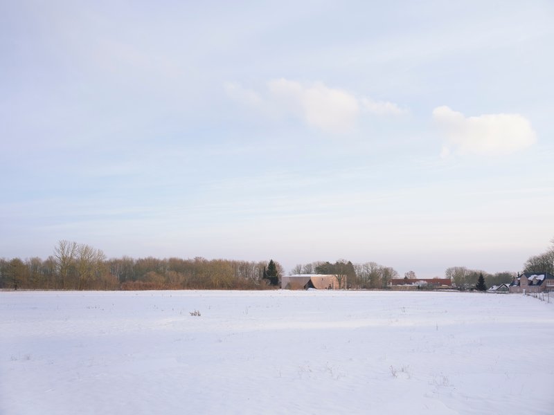 Distant view of the structure across an expansive snowfield with a tree line on the horizon