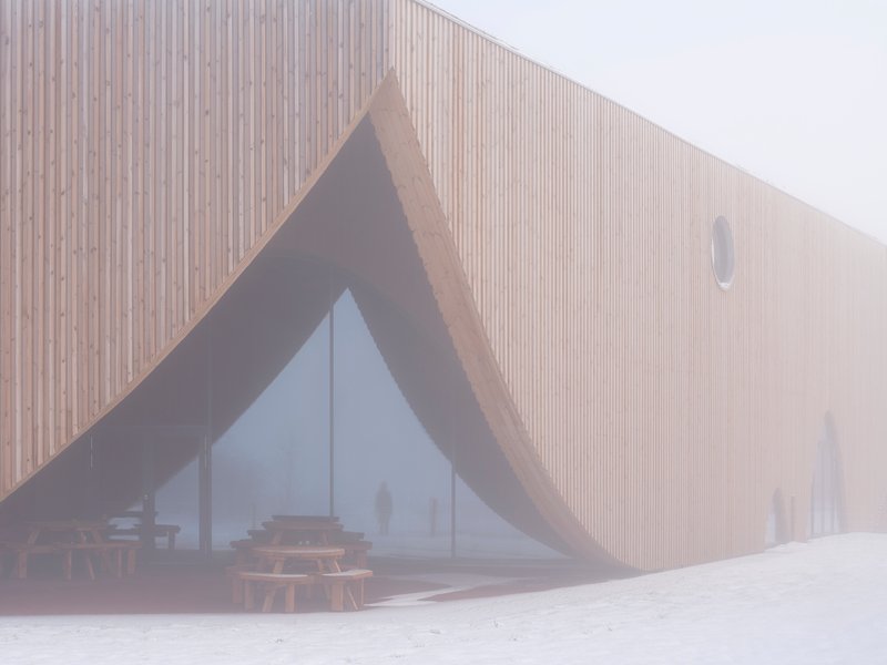 Timber-clad facade with triangular glazed entrance in heavy fog and fresh snow