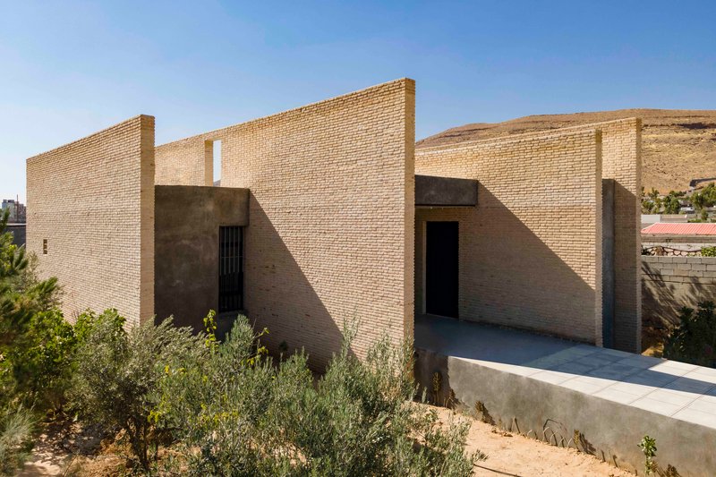 Elevated view of brick facade with triangular wall geometries and concrete volumes casting midday shadows