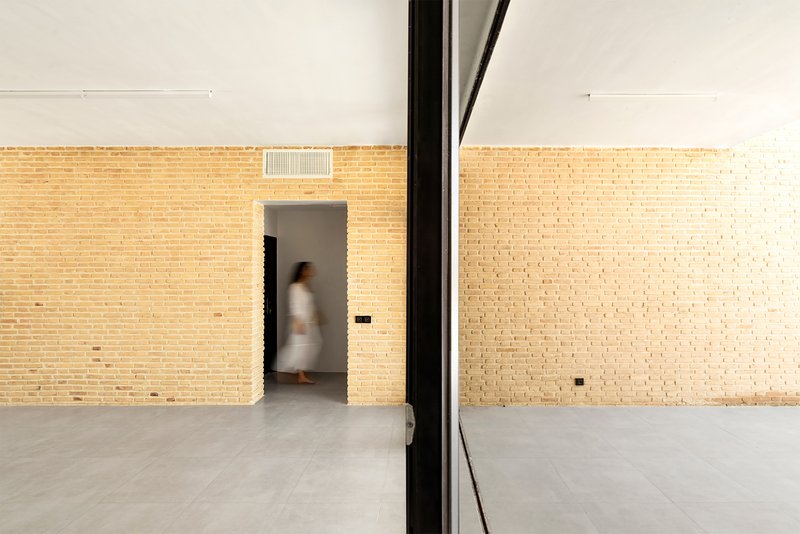 Interior room with pale brick walls and a doorway framing a figure passing through in motion