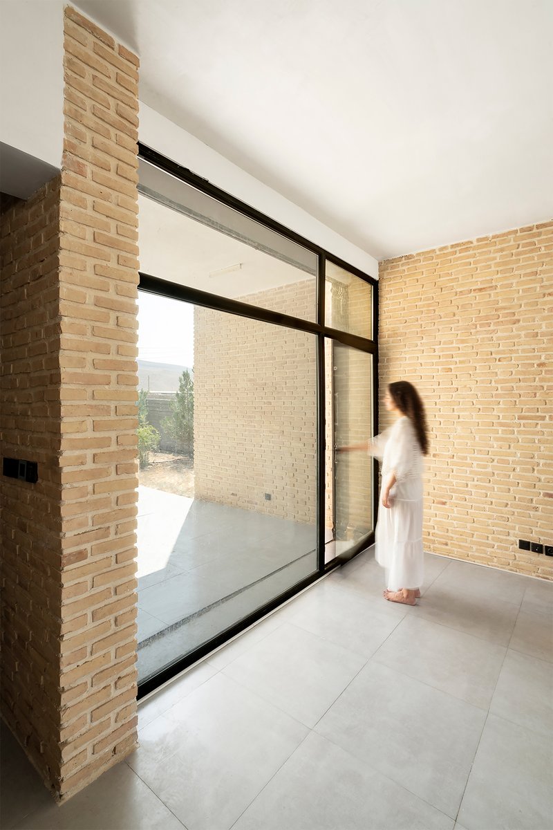 Corner glazed door with black steel frame opening to a brick-walled courtyard as a figure approaches