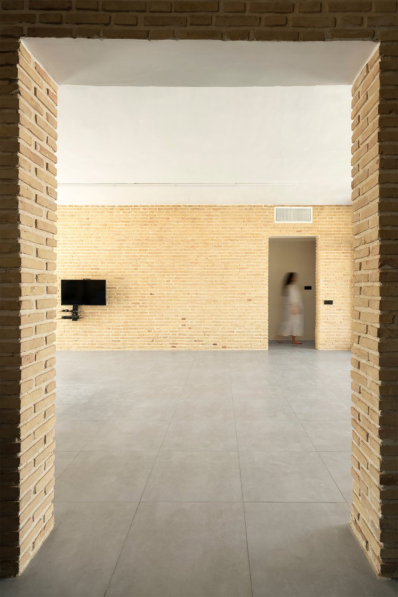 Double-height space framed by brick piers with clerestory light washing the buff masonry wall beyond