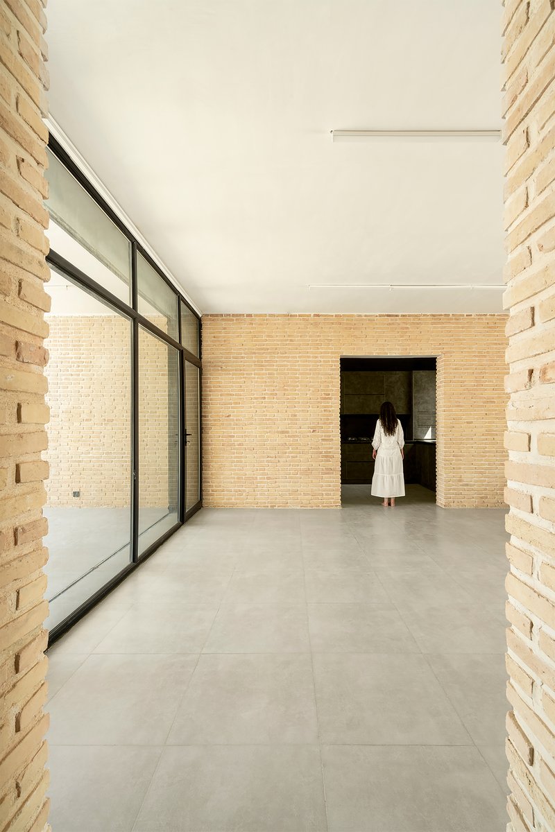 Open room with steel-framed glazing along one wall and a figure walking toward a darkened doorway
