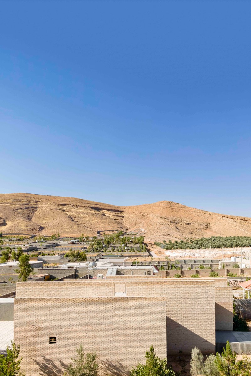 Rooftop view of the rectilinear brick structure amid a sparse settlement below arid mountains