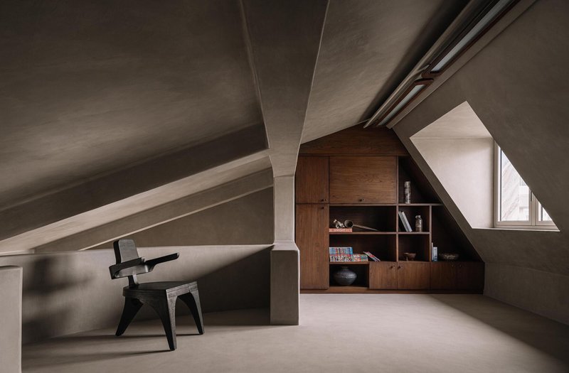 Attic workspace with exposed pitched ceiling beams and a built-in timber bookshelf under a triangular window