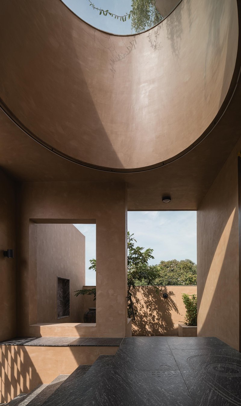 Interior courtyard with curved plaster walls and circular skylight framing trees beyond in sunlight
